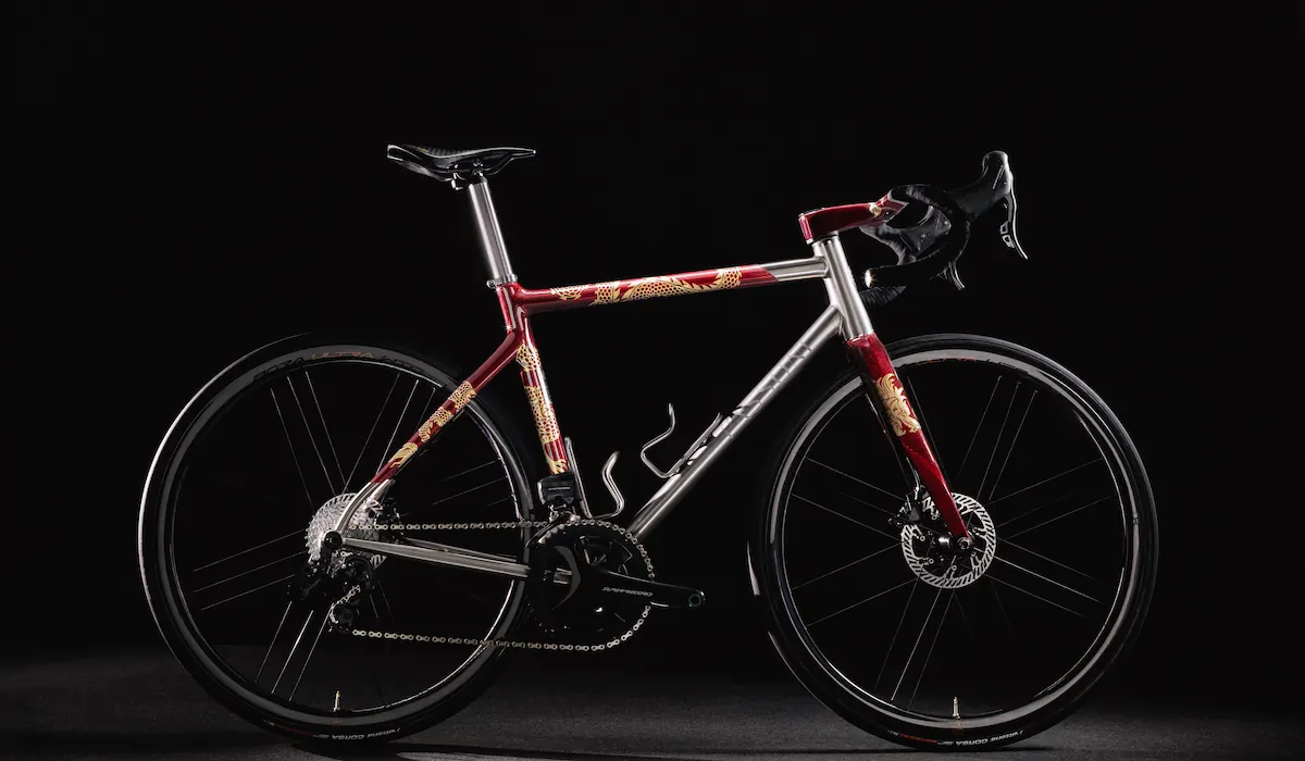 Titanium road bike with red and gold dragon paintwork, lit against a black background